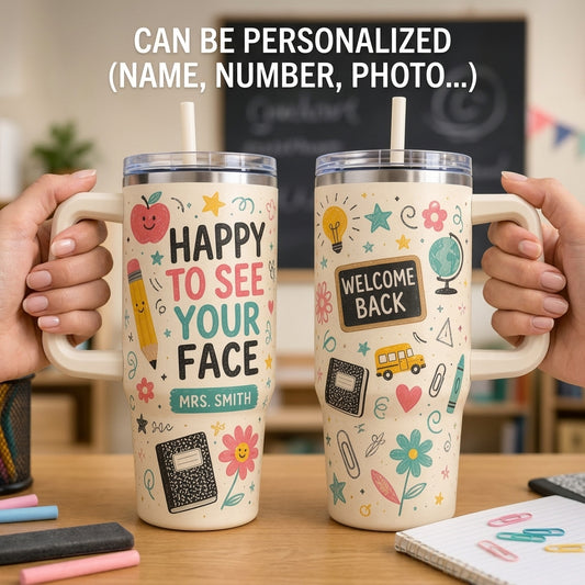 Two personalized stainless steel handled tumblers with clear lids and straws, held by hands on a desk. The left tumbler says 'HAPPY TO SEE YOUR FACE' with a name 'MRS.