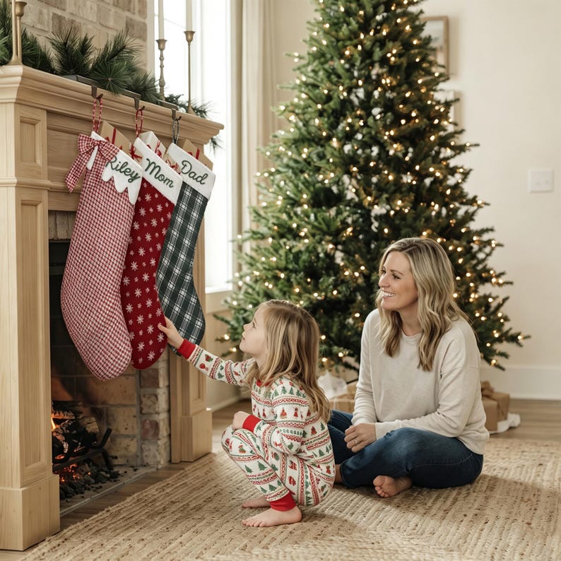 May include: Three Christmas stockings hanging from a fireplace mantel. The first is red and white gingham with a bow, the second is red with white snowflakes, and the third is green and black plaid. Each has a white cuff with embroidered names.