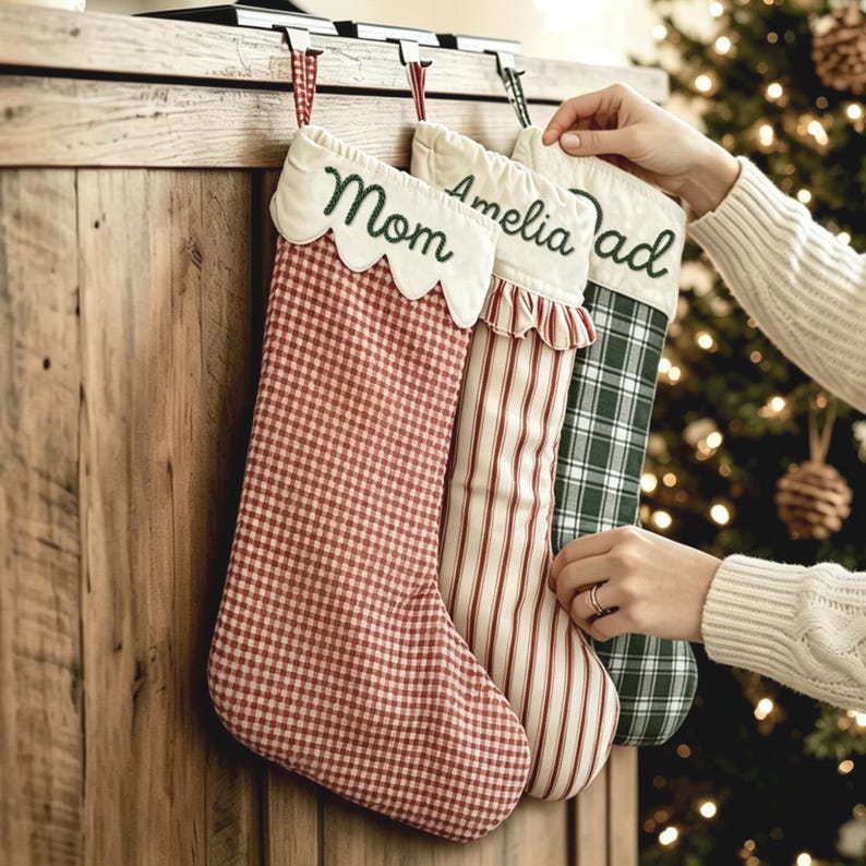 May include: Three Christmas stockings hanging from a wooden mantel. The first is red and white gingham with a scalloped cuff embroidered with Mom. The second has red and white vertical stripes. The third is green and white plaid with Dad embroidered.